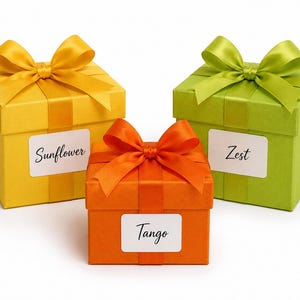 May include: Three square gift boxes in yellow, orange, and green, each with a matching satin ribbon bow. The boxes have white labels with the words "Sunflower", "Tango", and "Zest".