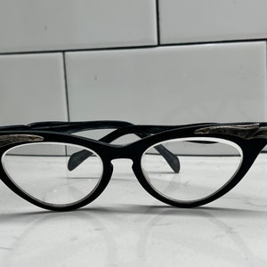May include: Black cat-eye glasses with silver accents on the frames.