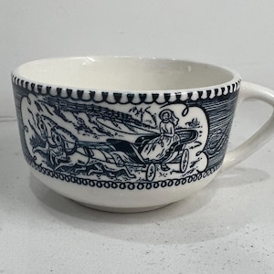May include: A white ceramic teacup with a blue and white floral pattern. The pattern features a woman riding in a carriage pulled by horses.