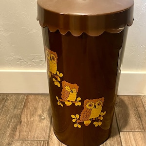 Könnte beinhalten: Ein brauner Vintage-Mülleimer mit einem gewellten Rand und einem Deckel. Der Mülleimer zeigt drei Eulenillustrationen in Gelb und Orange. Der Mülleimer besteht aus einem strapazierfähigen Material und eignet sich für verschiedene Räume.