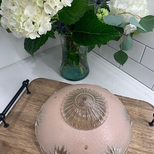 May include: A pink glass ceiling light fixture with a clear glass center dome. The light fixture has a scalloped edge and a floral design.