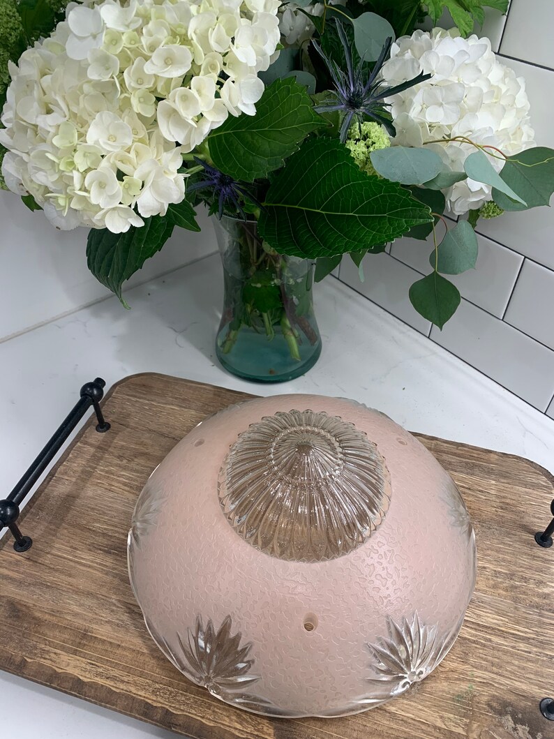 May include: A pink glass ceiling light fixture with a clear glass center dome. The light fixture has a scalloped edge and a floral design.