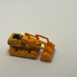 Pu&ograve; includere: Un bulldozer giocattolo giallo con un sedile nero e una benna gialla sollevata.