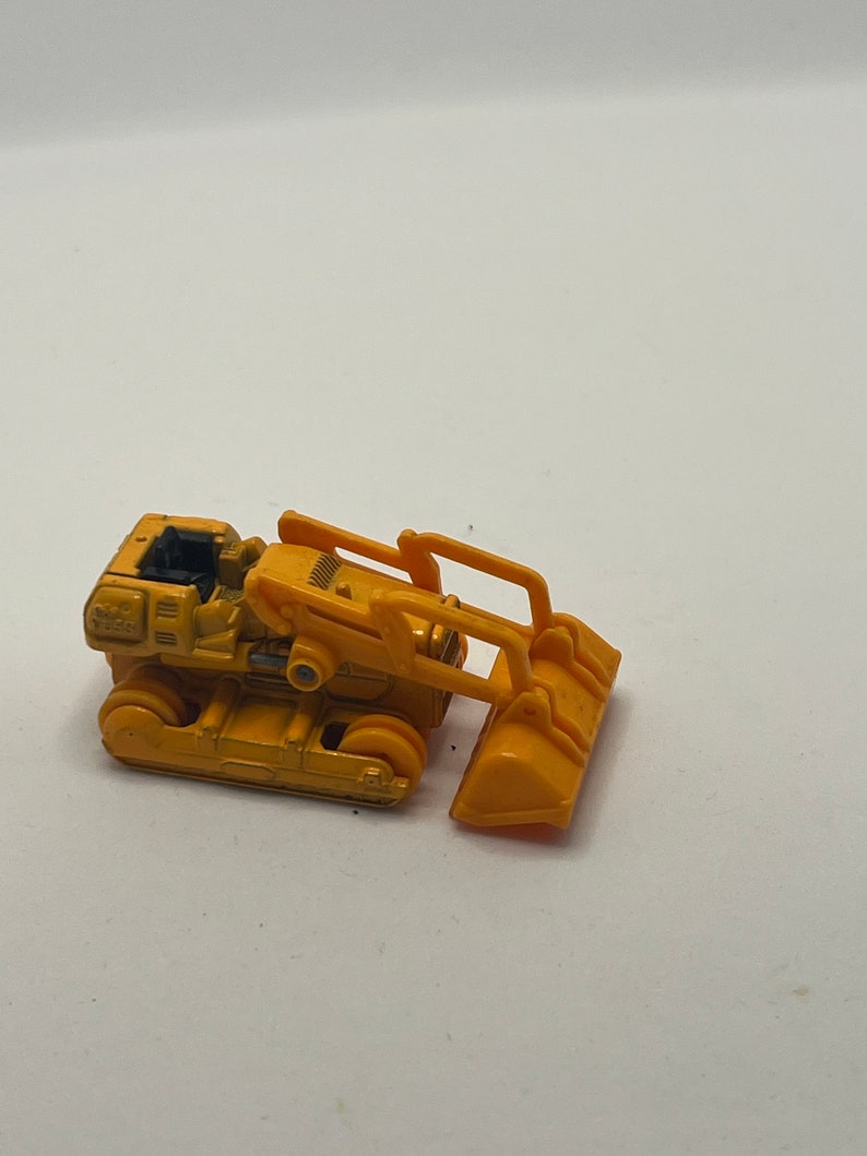 Pu&ograve; includere: Un bulldozer giocattolo giallo con un sedile nero e una benna gialla sollevata.