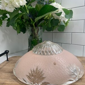 May include: A pink glass ceiling light fixture with a clear glass top and a textured surface. The light fixture has a decorative design around the edge.