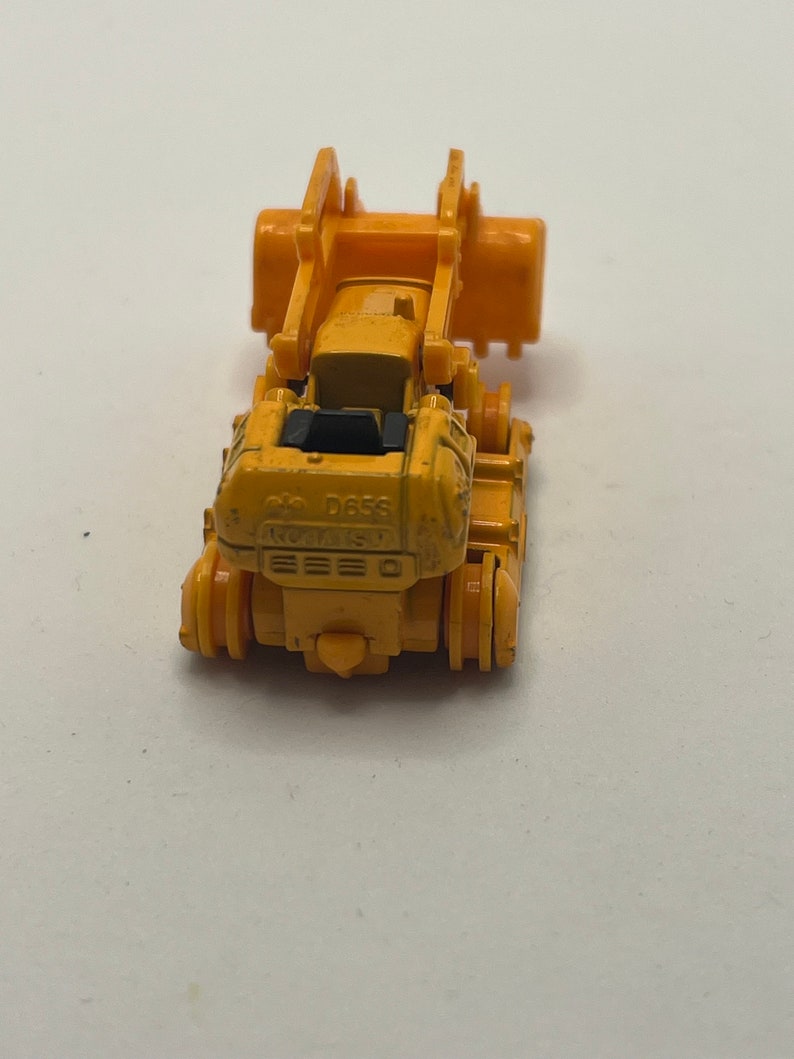 Pu&ograve; includere: Un bulldozer giocattolo giallo con un sedile nero e il testo "D655" sul lato.