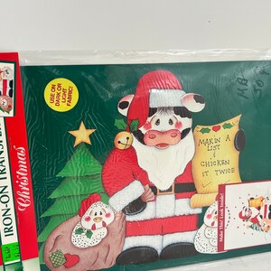 May include: Iron-on transfer design for a Christmas craft project featuring a cow dressed as Santa Claus holding a scroll that says "Makin a list & chicken it twice". The design also includes a Christmas tree and two chickens.