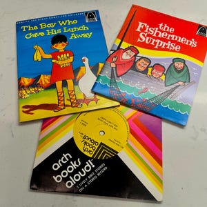 May include: Three vintage children's books and a record. The books are titled "The Boy Who Gave His Lunch Away" and "The Fishermen's Surprise." The record sleeve has the text "arch books aloud!" and "2 Lively Bible Stories on a Stereo Record."