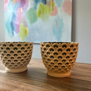 May include: Two cream-colored ceramic planters with a green geometric pattern. The planters have a scalloped design and a rounded base.