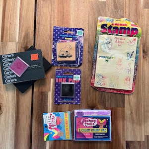 May include: A collection of craft supplies including a black Carter's ink pad, a purple-packaged rubber stamp with a bear graphic, a purple-packaged black ink pad, a Lisa Frank rubber stamp set, and two Fantasy Trolls 2-colour stamp pads in purple.