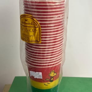 May include: A stack of red and white striped cold cups in a plastic bag. The cups have a Snoopy character design on the bottom. The label reads "Hallmark 25 - 5 OZ COLD CUPS".