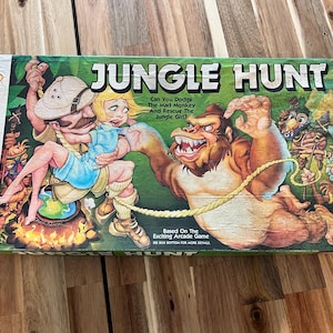 May include: A vintage Jungle Hunt board game box. The box features a colorful illustration of a man and a woman being chased by a gorilla. The text "JUNGLE HUNT" is prominently displayed. Ages 7-14, for 2 to 4 players.
