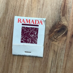 May include: A white matchbook with the word "RAMADA" printed in red letters. The matchbook has a red and white graphic design and the text "EDDY MATCH 1-800-287-3168".