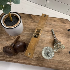 May include: A wooden tray with black metal handles, featuring a potted plant, a brass door plate, and three antique door knobs. Two of the knobs are brown and one is clear glass.