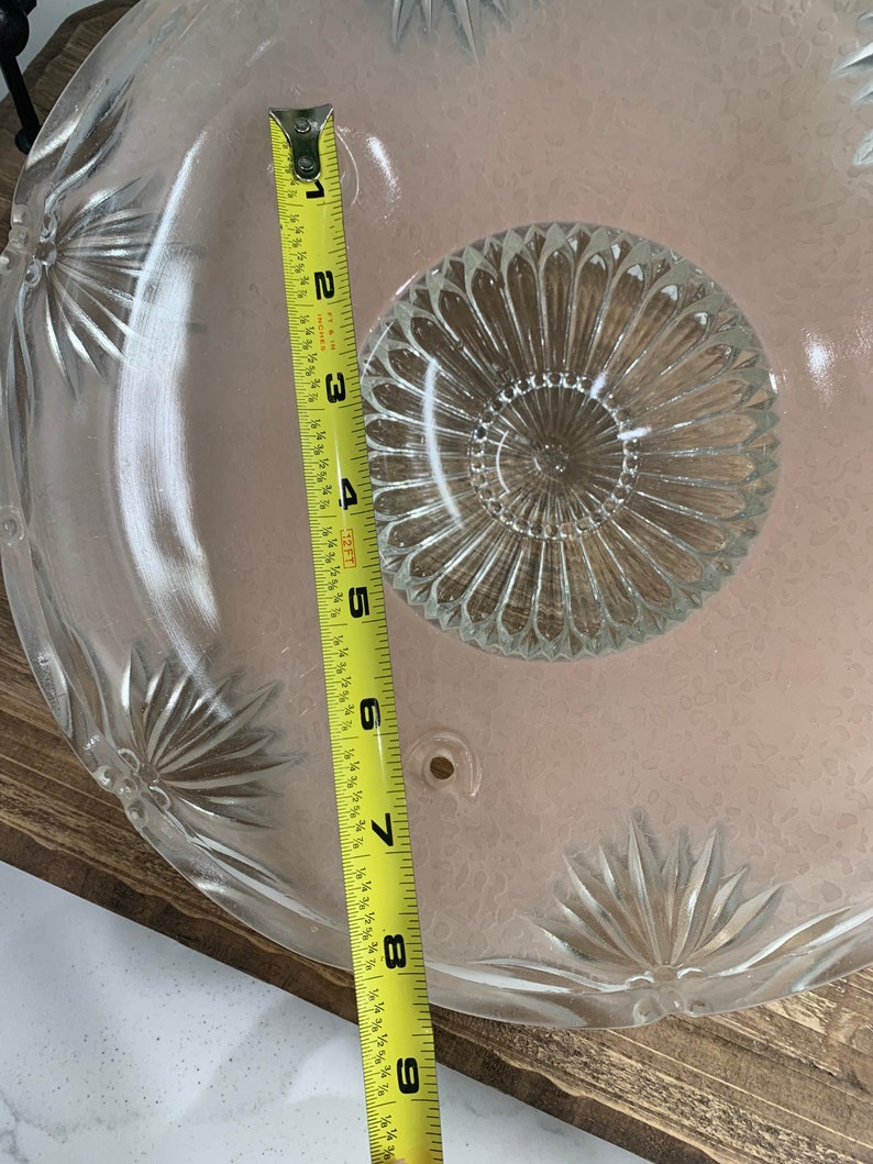 May include: A clear glass ceiling light fixture with a scalloped edge and a central, circular, textured design. The fixture measures 9 inches in diameter.