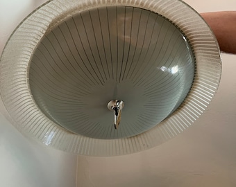 May include: A white ceiling light fixture with a frosted glass shade and a decorative metal ring around the edge. The shade has a radial pattern of lines.
