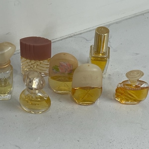 May include: A collection of six miniature perfume bottles with various shapes and caps, containing golden-coloured liquid. The bottles feature different designs, including one labelled Dazzling and another labelled Beautiful, with clear glass bodies.