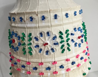 May include: A bell-shaped pendant light fixture with a white, textured, carved surface. The exterior is decorated with small, translucent plastic pins in blue, green, pink, and red, arranged in floral and geometric patterns across the vertical panels.