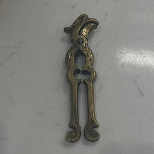 May include: A gold-toned metal nutcracker shaped like a bird with a detailed design. The nutcracker has a hinged jaw and a decorative handle.