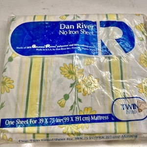 May include: A twin-size fitted sheet in a plastic package. The sheet features a white background with yellow and green vertical stripes and yellow floral patterns. The packaging includes the text "Dan River No Iron Sheet."