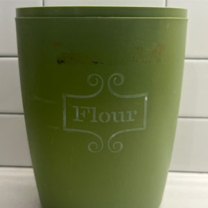 以下が含まれることがあります： 装飾的なフォントで「Flour」と書かれた白いラベルが付いた緑色のプラスチック製容器です。