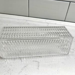 May include: A clear, rectangular, decorative box with a diamond-patterned design. The box is made of a transparent material and has a lid. The box is approximately 6 inches long, 2 inches wide, and 2 inches tall.