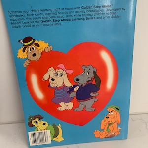 May include: A book cover with a blue background and a large red heart. The heart has four cartoon dogs on it. The text on the cover reads "Golden Step Ahead" and "Golden Step Ahead Learning Series".