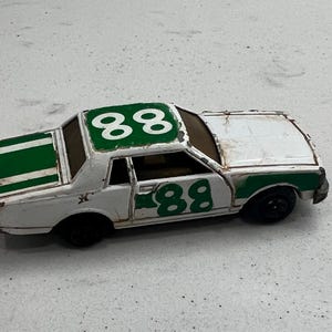 May include: A vintage toy race car, white with green accents, featuring the number "88" prominently displayed on the roof and sides. The car has black wheels and shows signs of wear.