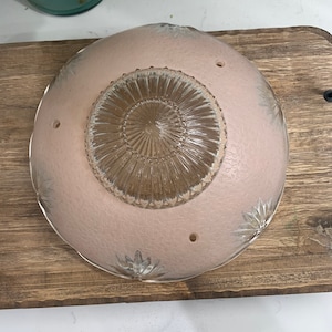 May include: A pink glass ceiling light fixture with a clear glass center and a floral design. The fixture has four holes for mounting.