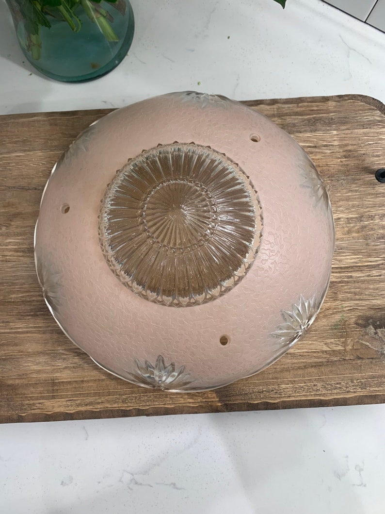 May include: A pink glass ceiling light fixture with a clear glass center and a floral design. The fixture has four holes for mounting.