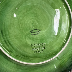 Pu&ograve; includere: Piatto in ceramica verde con bordo bianco e design circolare. Il fondo del piatto ha il testo "Prego Italia GmbH" e "Fatto a Mano Made in Italy" in nero. Il piatto ha anche il numero "8358/32 Made in Italy" in nero.