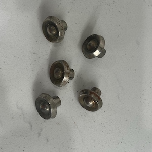 May include: Five small, silver-colored metal knobs with a rounded top and a short, cylindrical stem. The knobs are arranged on a light-colored surface, showing signs of wear and age.