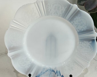 May include: A white milk glass plate with a scalloped edge and an embossed floral design. The plate is on a black metal stand.