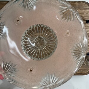 May include: A vintage glass light fixture shade with a pink tint and a clear, intricate design. The shade has four holes around the top edge.