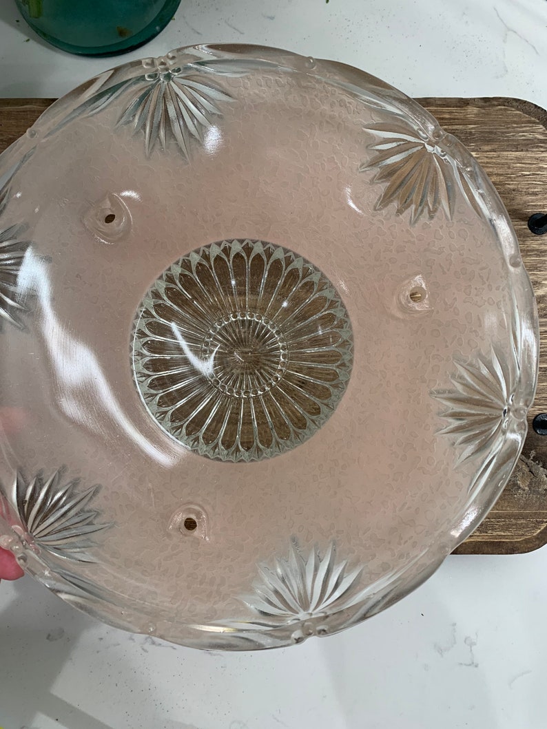 May include: A vintage glass light fixture shade with a pink tint and a clear, intricate design. The shade has four holes around the top edge.