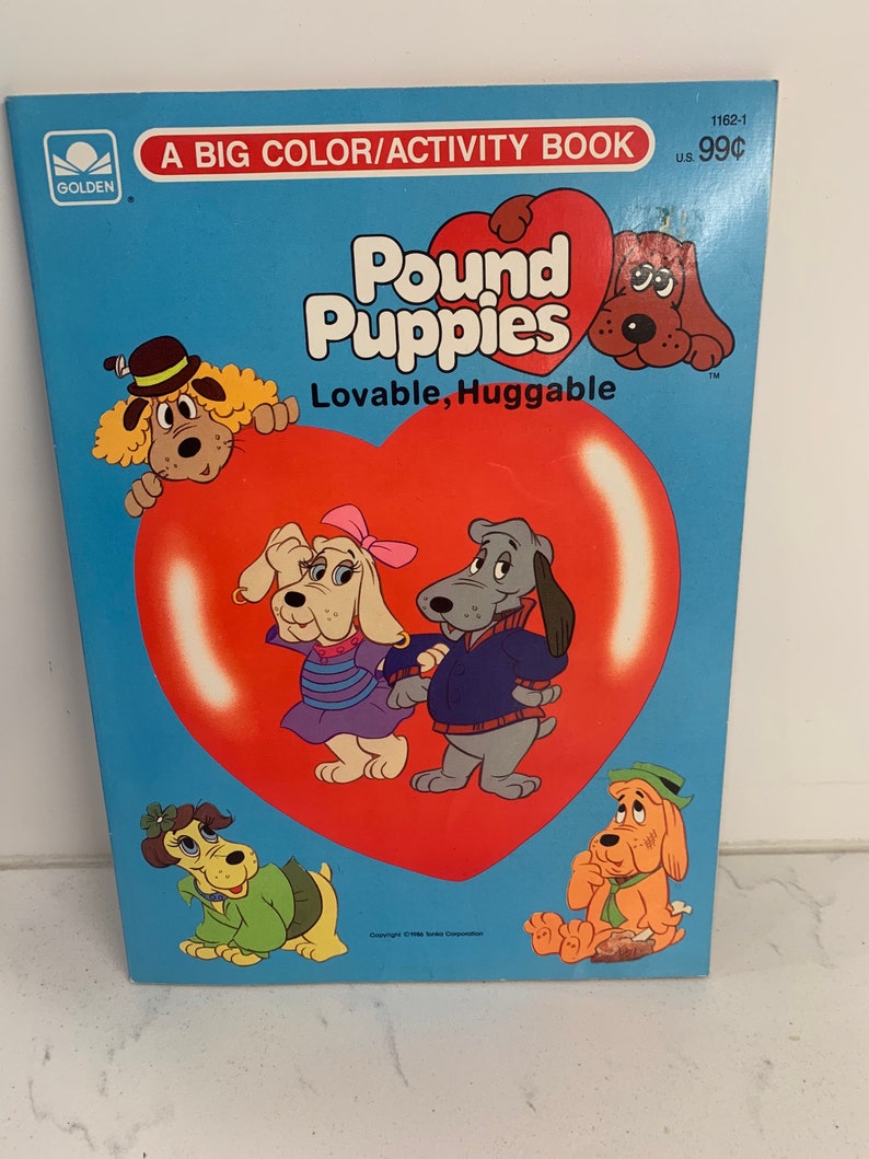 May include: A Golden Books activity book cover featuring the Pound Puppies cartoon characters. The cover is blue with a red heart in the centre. The title "Pound Puppies" is in large, colourful letters. The text "Lovable, Huggable" is below the title. The book is priced at 99 pence.