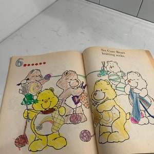 May include: A page from a children's book featuring six Care Bears knitting socks. The text on the page reads "Six Care Bears knitting socks."