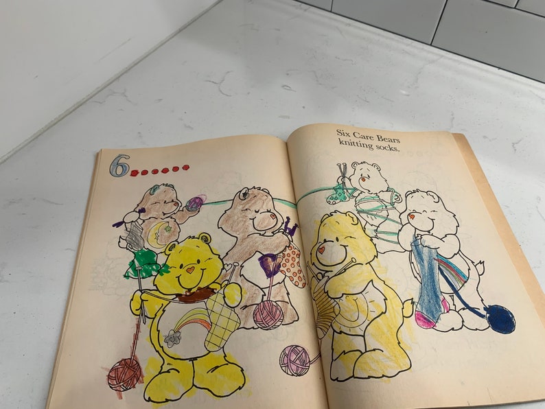 May include: A page from a children's book featuring six Care Bears knitting socks. The text on the page reads "Six Care Bears knitting socks."