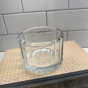 Könnte beinhalten: Ein klares Glasgefäß mit geriffeltem Design. Das Gefäß steht auf einem Stapel Bücher.