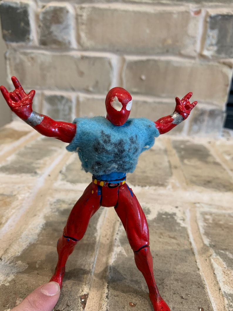 以下が含まれることがあります： 雪の結晶模様の青いシャツを着た、赤と青のスパイダーマンのアクションフィギュア。フィギュアは腕を伸ばし、足を広げてポーズをとっている。
