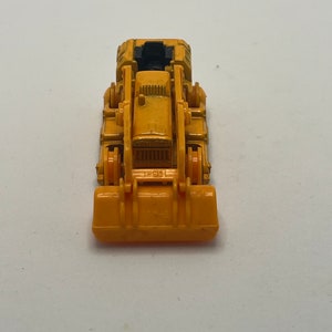 Pu&ograve; includere: Un bulldozer giocattolo giallo con un sedile nero e un caricatore frontale nero. Il bulldozer &egrave; su uno sfondo bianco.