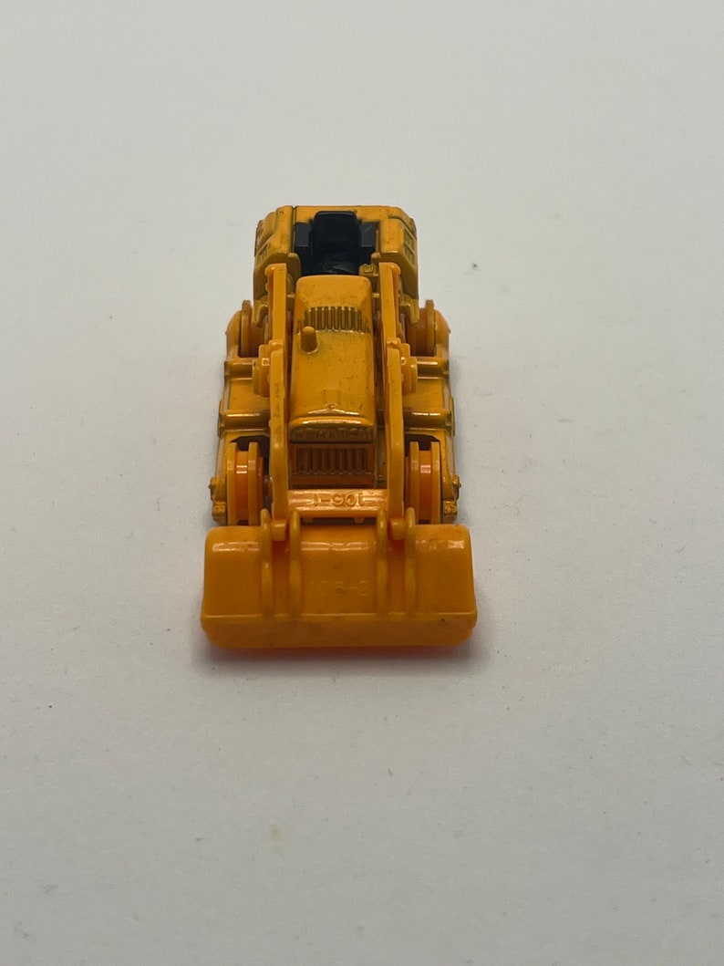 Pu&ograve; includere: Un bulldozer giocattolo giallo con un sedile nero e un caricatore frontale nero. Il bulldozer &egrave; su uno sfondo bianco.
