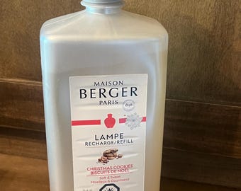 Könnte beinhalten: Eine durchsichtige Kunststoffflasche mit Maison Berger Paris Lampen-Nachfüllflüssigkeit im Duft Christmas Cookies. Das Etikett zeigt den Markennamen, ein rotes Symbol, eine Schneeflocke und den Text 1L-33.8 US fl.oz. mit einem Gefahrenhinweis.