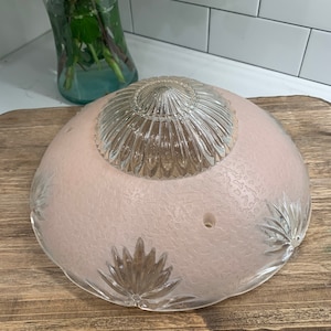 May include: A pink glass ceiling light fixture with a clear glass center and a decorative floral pattern around the edge.