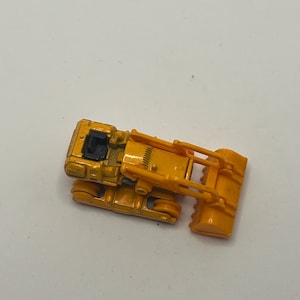 Pu&ograve; includere: Un bulldozer giocattolo giallo con una cabina nera e una pala gialla sollevata.