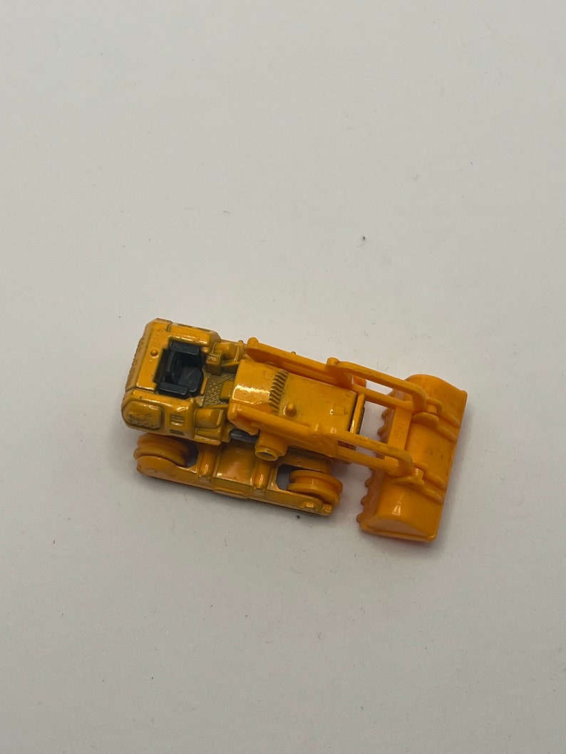 Pu&ograve; includere: Un bulldozer giocattolo giallo con una cabina nera e una pala gialla sollevata.