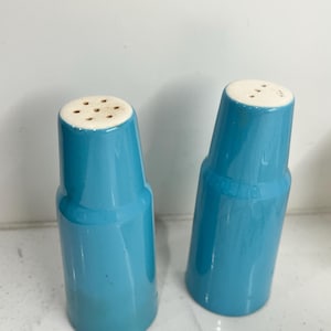 May include: A set of two blue ceramic salt and pepper shakers with white tops. The shakers have a simple, cylindrical design.