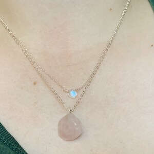 May include: A silver chain necklace with two pendants. The top pendant is a small, iridescent moonstone. The bottom pendant is a larger, teardrop-shaped rose quartz.