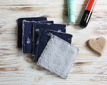 May include: A stack of four reusable makeup remover pads, two are navy blue with a floral pattern and two are gray. The pads are on a white wooden surface with a tube of face cream, a tube of lipstick, and a heart-shaped bar of soap.