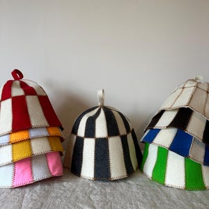 May include: Three conical felt sauna hats with vertical striped patterns. The left stack features red, orange, yellow, and pink stripes. The centre hat is black and white. The right stack displays black, blue, and green stripes with white.